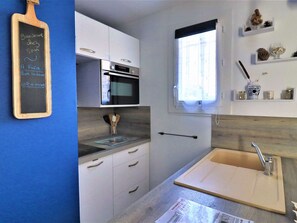 Uma cozinha moderna com armários brancos, forno embutido, janela com persianas e bancada de madeira.