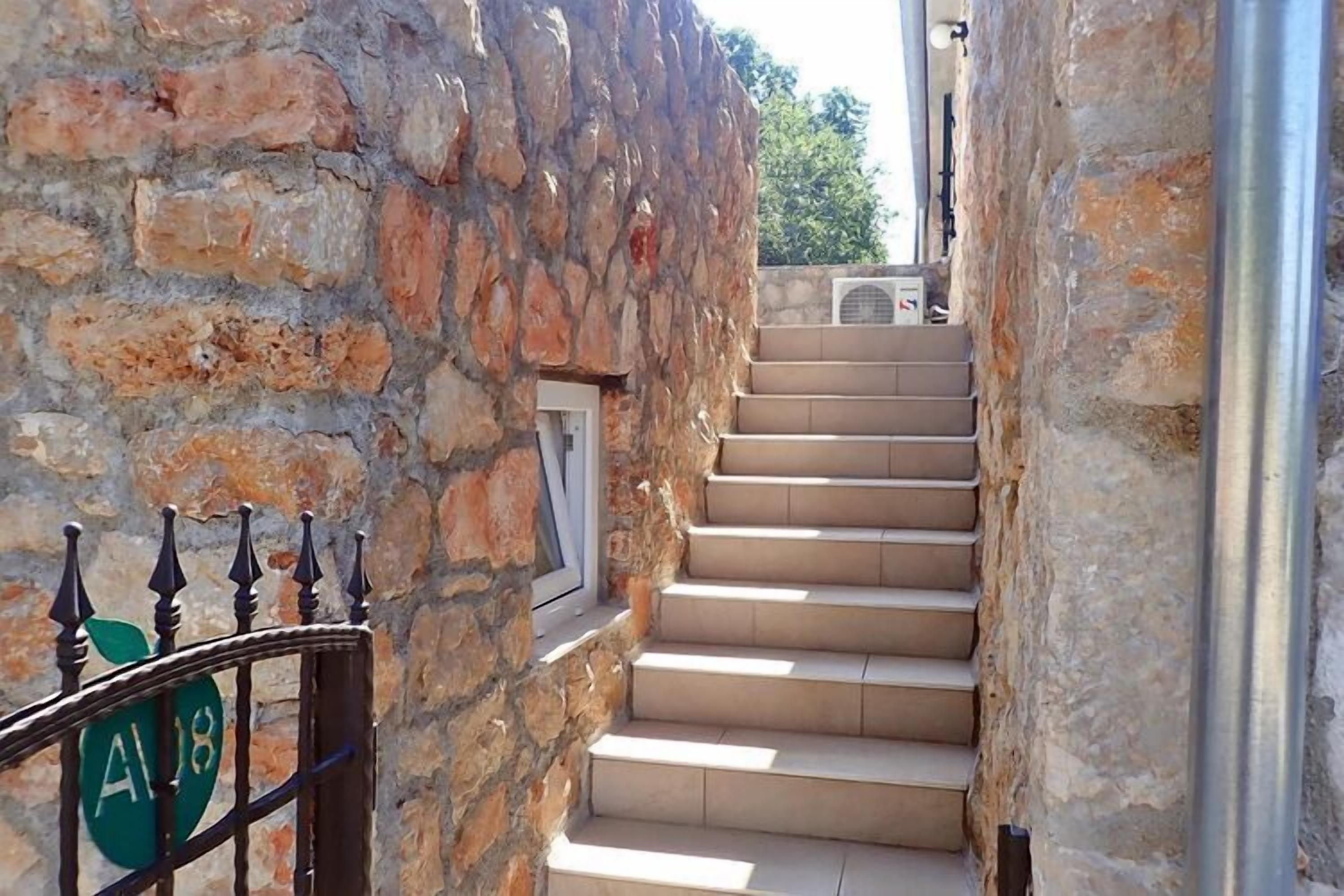 A stone staircase leading to a door with a metal gate, a window, and a metal pipe on the right.