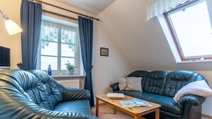 Ein Wohnzimmer mit einem schwarzen Ledersofa, einem Holztisch und einem Fenster mit Vorhängen.