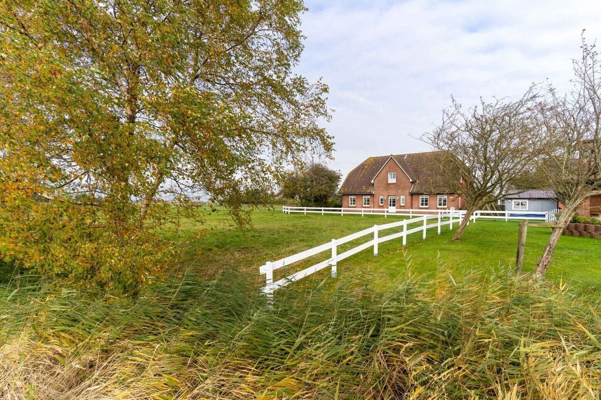 A rural property with a large brick house, white fence, and surrounding greenery.