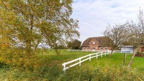 Ein ländliches Anwesen mit einem großen Backsteinhaus, einem weißen Zaun und umgebender Bepflanzung.
