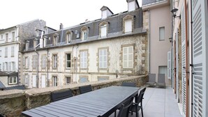 A terrace with a long table and chairs, overlooking a row of buildings with traditional architecture and shutters. - Beautiful T3 apartment with terrace and Wi-Fi in the center of La Bourboule (La Bourboule)