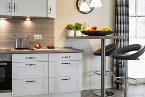 Eine moderne Küche mit weißen Schränken, einem Edelstahltoaster, einer Obstschale und einer Uhr an der Wand.