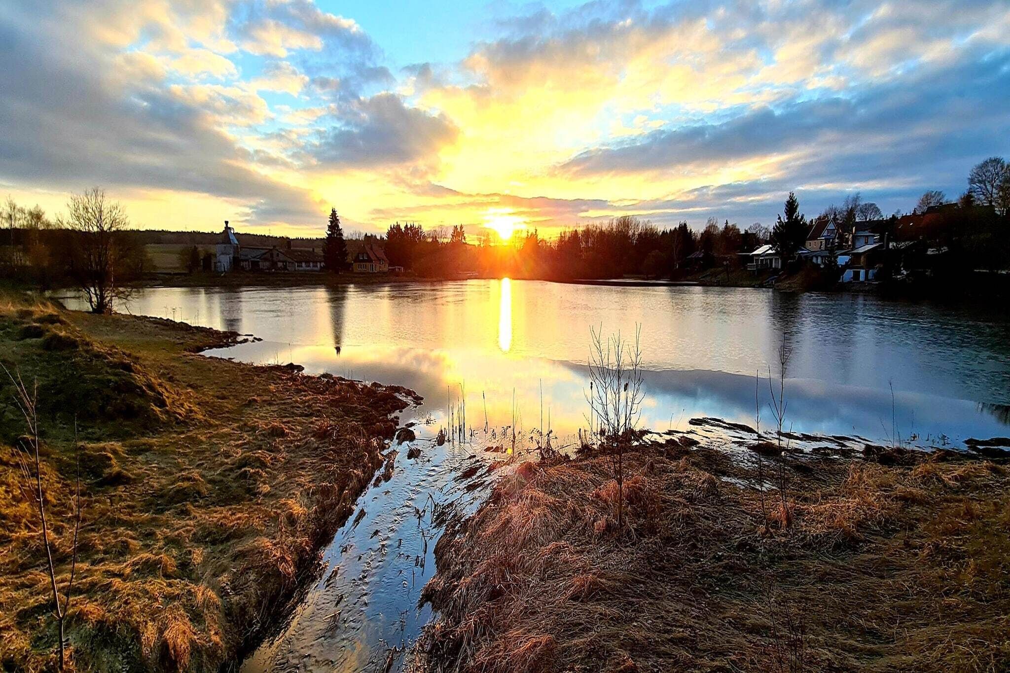 Una vista serena d'un llac al capvespre, amb aigües tranquil·les i cases a la distància.