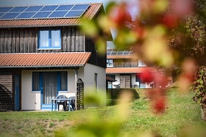 Un bâtiment à deux étages, doté de panneaux solaires sur le toit, d’une fenêtre à cadre bleu et d’un petit patio avec une table et des chaises.