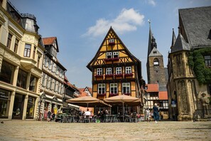A cobblestone square with traditional half-timbered buildings, outdoor seating, and a church spire.