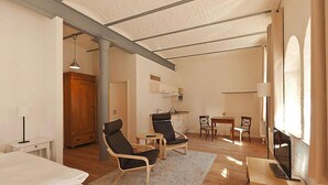 A spacious living room with a large window, a flat-screen TV, and a wooden dining table. - Appartements im Sudhaus in Schwerin (Schwerin)