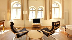 A room with a wooden floor, two black leather chairs, a small round table, a television on a wooden stand, and two windows with arched tops. - Appartements im Sudhaus in Schwerin (Schwerin)