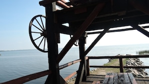 A wooden deck with a wooden table and a wheel structure, overlooking a calm body of water. - Holiday Home Sulomino with Private Beach (Sulomino)