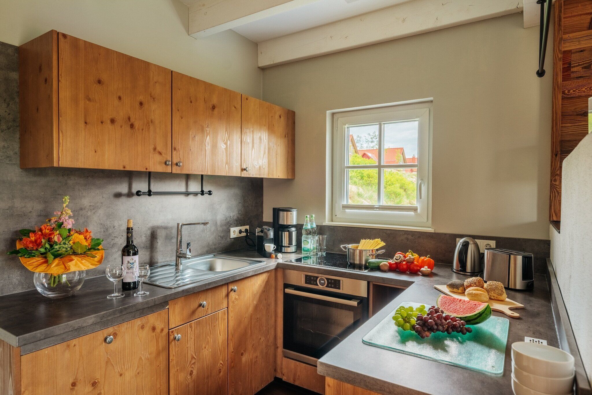 Een moderne keuken met houten kastjes, een inbouwoven, een koffiezetapparaat en een raam met uitzicht op groen.