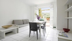 Een moderne, minimalistische woonruimte met een eethoek, een bank en uitzicht op het groen.