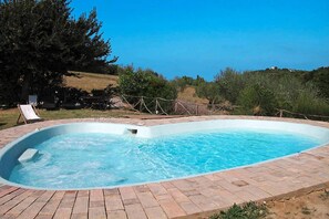 A rectangular swimming pool with a brick border, surrounded by a grassy area and trees.