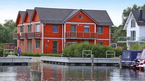 Une maison rouge à deux étages, dotée d’un balcon, d’un quai et d’un petit bateau.