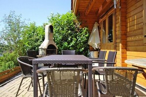Relax on the patio surrounded by lush greenery, with a barbecue grill and comfortable seating for a casual outdoor meal.
