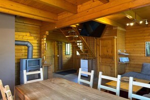 Cozy cabin-style interior with a rustic aesthetic, featuring a dining table, bench, kitchenette, and staircase to an upper level.