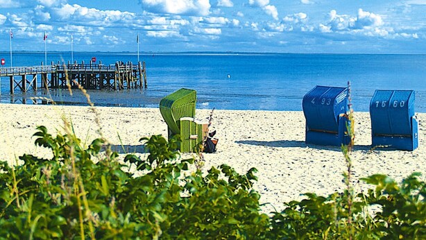 A beach with a pier, green and blue beach chairs, and a clear blue sky.