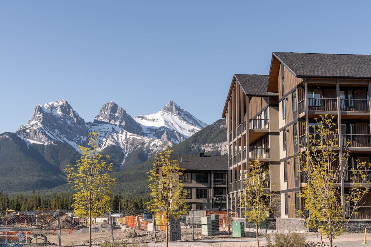 A modern building with multiple balconies, set against a backdrop of snow-capped mountains.