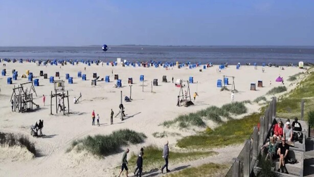A beach with numerous blue and white beach chairs and umbrellas, a lifeguard tower, and a sandy walkway.