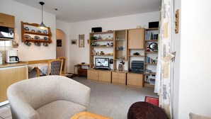 A cozy living room with a sofa, a coffee table, a TV, and a bookshelf. - Gemütliche Ferienwohnung Dornumersiel (Dornumersiel)