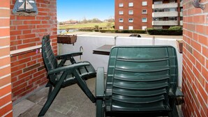 A patio area with a green chair and a table, a brick wall, and a view of a building in the background.