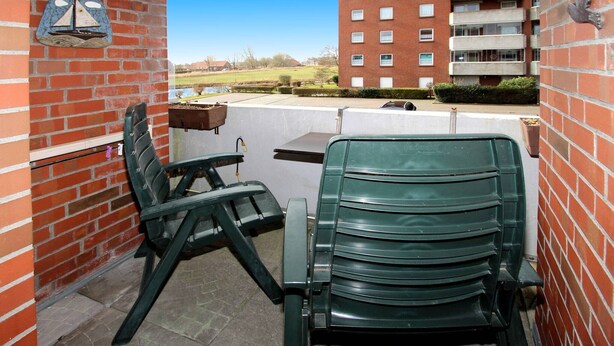A patio area with a green chair and a table, a brick wall, and a view of a building in the background. - Gemütliche Ferienwohnung Dornumersiel (Dornumersiel)