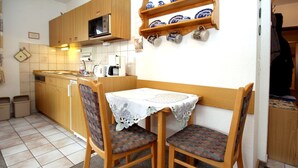 A compact kitchen with wooden cabinets, a microwave, and a small dining table with two chairs.