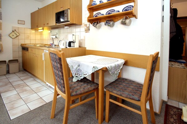 A compact kitchen with wooden cabinets, a microwave, and a small dining table with two chairs.