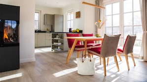A modern kitchen with a dining area featuring red chairs and a wooden table. - Reetdachhaus am Bodden mit Sauna (Fuhlendorf)