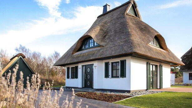 A traditional thatched-roof house with a white exterior, green shutters, and a small front garden. - Reetdachhaus am Bodden mit Sauna (Fuhlendorf)