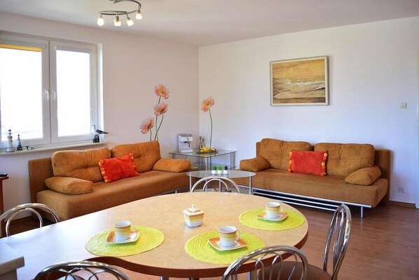 A modern living room with two sofas, a dining table with placemats, and a painting on the wall.