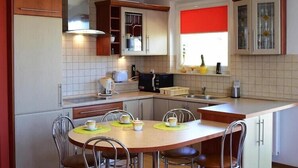 A compact kitchen with a dining area, featuring a sink, stove, cabinets, and a window with a red blind. - Apartment in Ustka near Baltic Sea Beach (Ustka)
