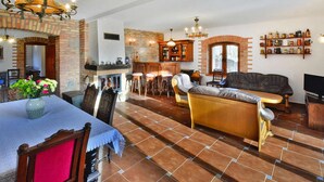 Un vaste salon doté d’une cheminée, un coin repas avec une table et des chaises, et une cuisine avec un bar.