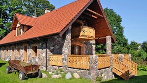 Une cabane en pierre et en bois, avec un toit recouvert de tuiles rouges, un balcon en bois et une charrette en bois à l’extérieur.