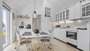 Una cocina moderna con armarios blancos, una mesa de comedor con sillas y una lámpara colgante.