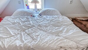 Una cama bien hecha con un edredón blanco, una lámpara y una ventana con vistas al exterior.