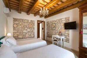 Une chambre avec deux lits, des murs en pierre, un lustre, une télévision et une petite table avec une chaise.