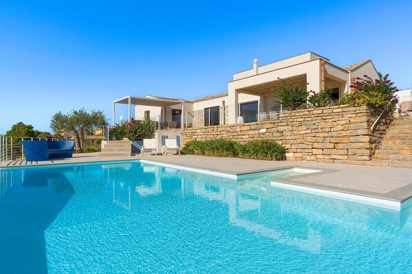 Une maison moderne dotée d’une piscine, de murs en pierre et d’un espace salon extérieur.