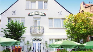 A white building with a sign reading "GUD KOOB" and a balcony with a wrought iron railing.