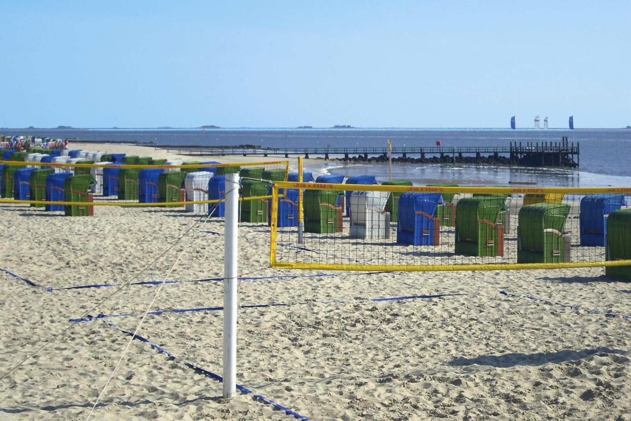 A beach volleyball court with a net, surrounded by beach chairs and umbrellas.