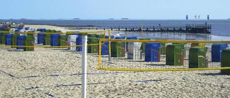 A beach volleyball court with a net, surrounded by beach chairs and umbrellas.