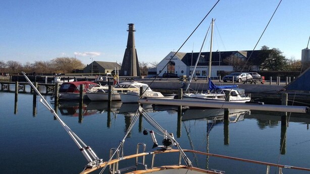 A marina with boats docked, a lighthouse, and buildings in the background.
