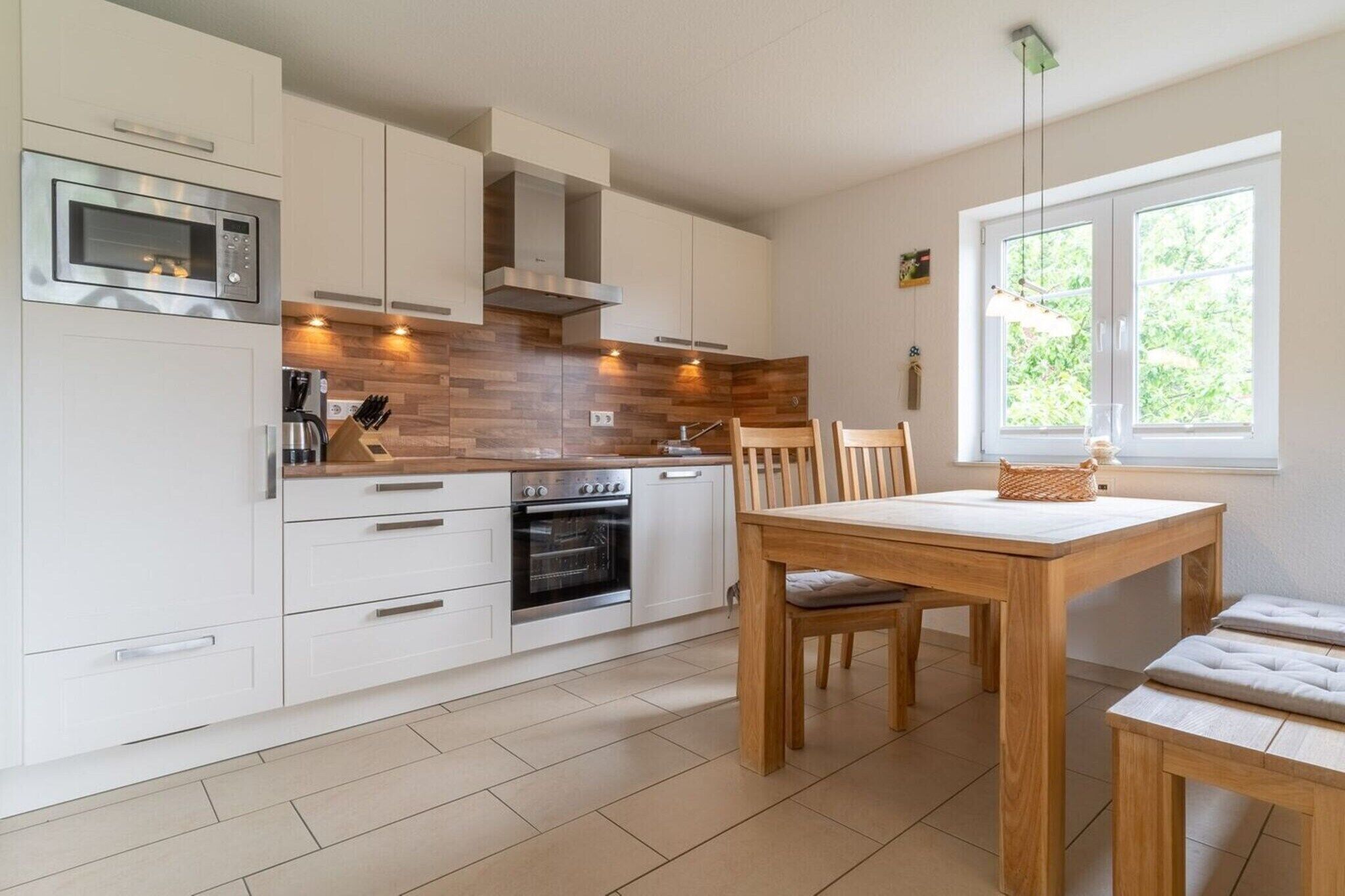 Une cuisine moderne avec des meubles blancs, un four encastré et un coin repas comprenant une table et des chaises en bois.
