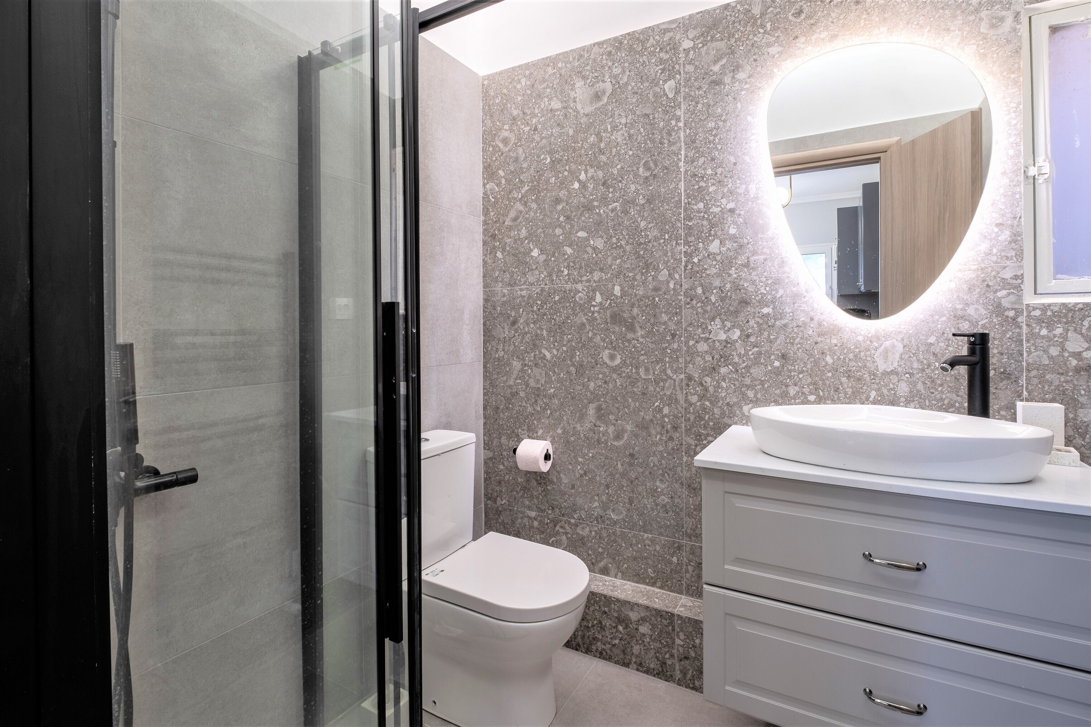 Une salle de bain avec une porte de douche en verre, des toilettes, un lavabo avec un miroir et un mur en marbre.