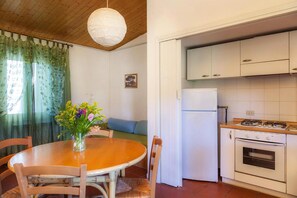 A kitchen with white cabinets, a stove, and a refrigerator. There is a dining table with chairs and a vase of flowers.