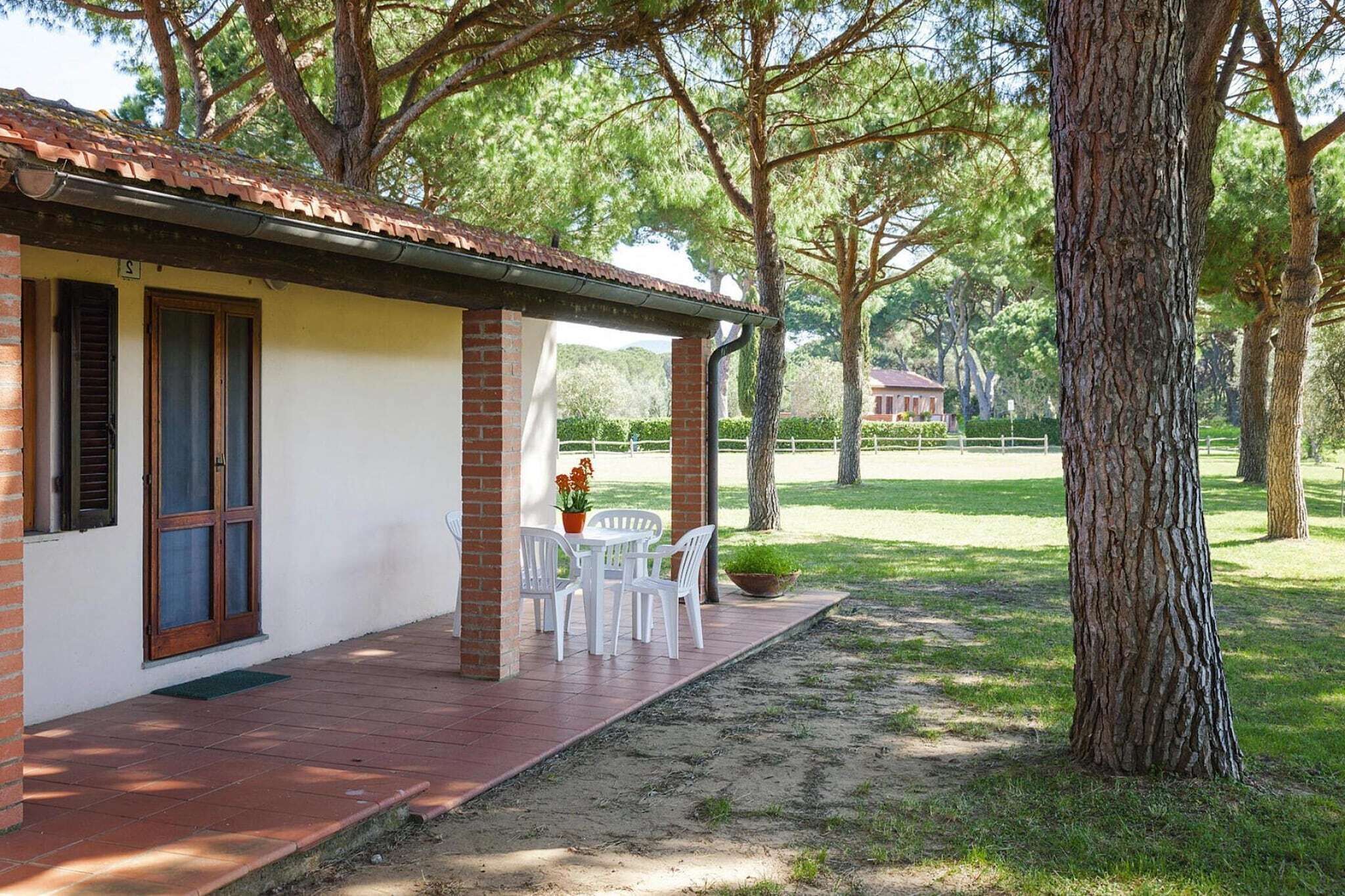 Un petit bâtiment avec un toit en tuiles, une colonne en briques et un patio couvert avec des chaises et une table blanches.
