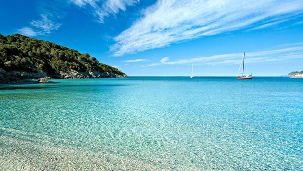A clear blue sea with a boat and a sailboat in the distance, surrounded by a rocky coastline. - Apartment near Grosseto beaches and pine forest (Marina di Grosseto)