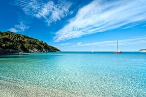 A clear blue sea with a boat and a sailboat in the distance, surrounded by a rocky coastline.