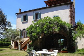 A two-story house with a covered outdoor seating area, a staircase, and a large arched doorway.