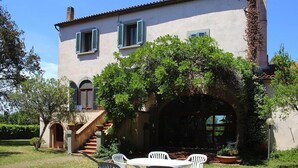 A two-story house with a covered patio, outdoor seating, and a staircase leading to the entrance. - Apartment near Grosseto beaches and pine forest (Marina di Grosseto)