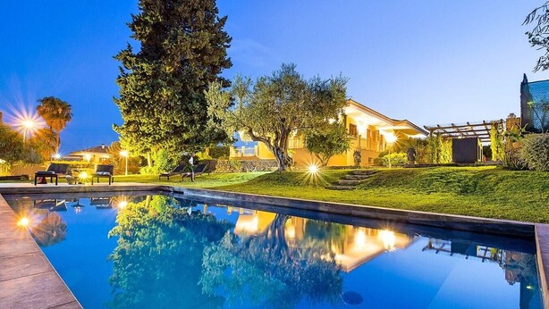 A swimming pool with a clear reflection, surrounded by a well-maintained lawn and trees.